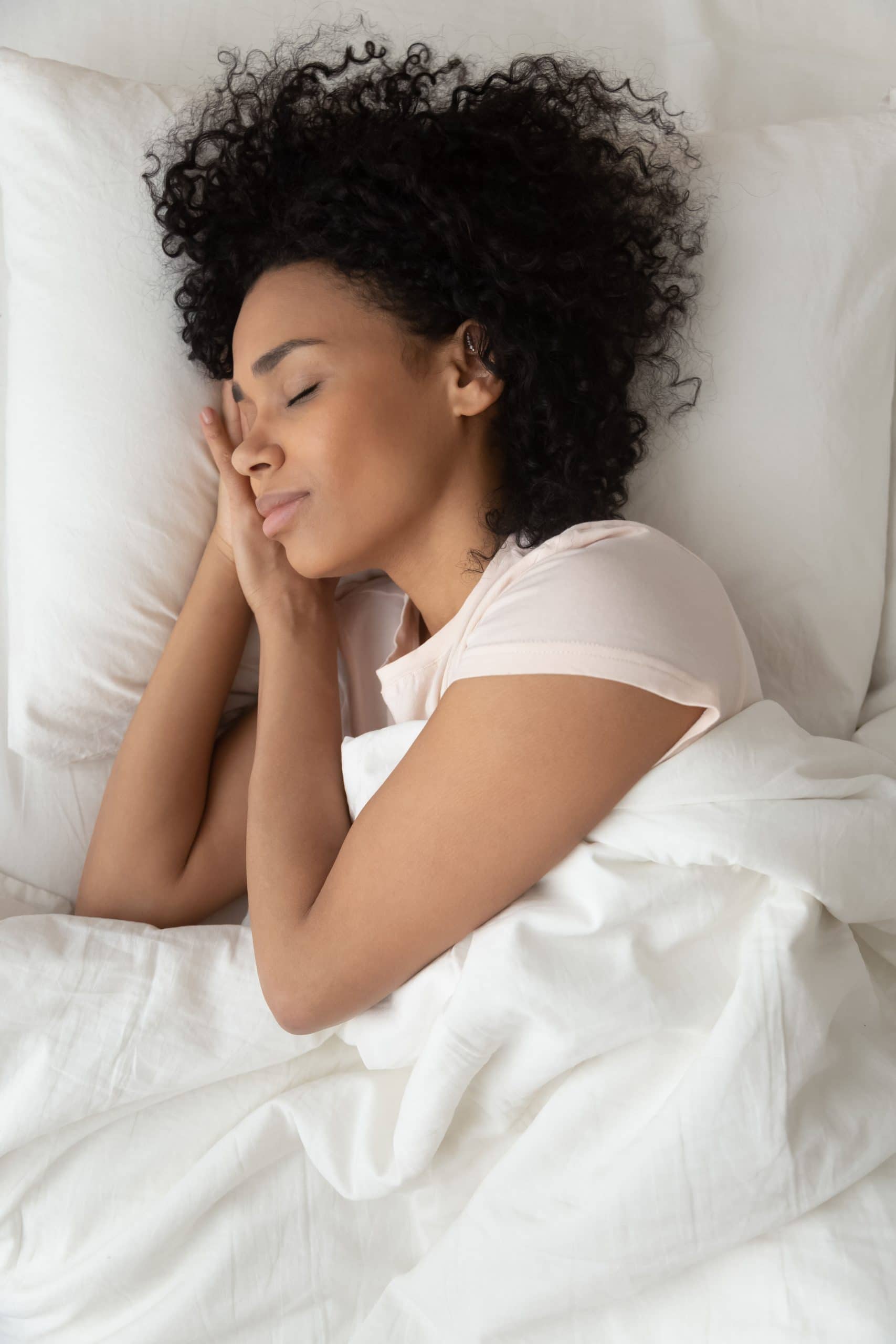 Top view of peaceful african American young woman lying in comfortable bed sleeping on white sheets, calm biracial black millennial girl relaxing napping in cozy bedroom seeing dreams or daydreaming